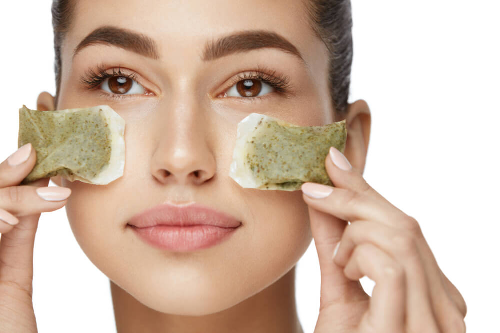 woman holding tea bags under eyes